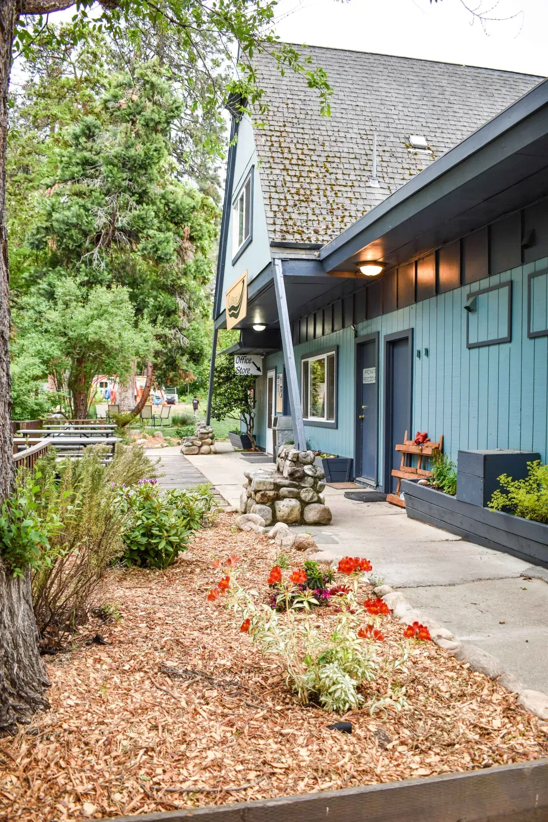 Blue house with a flower bed and front walkway under trees