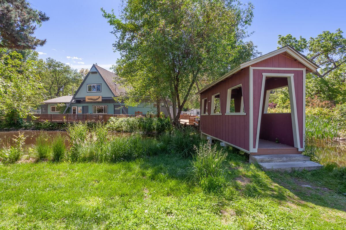 Red shed in a grassy yard with a house and trees in the background