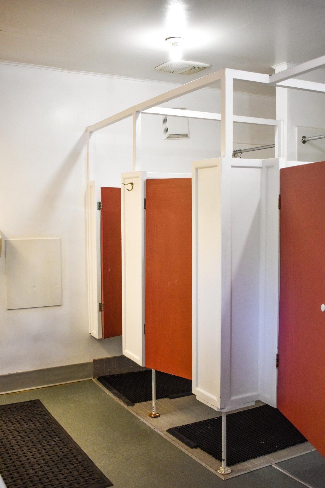Public restroom stalls with open red doors and white partitions on green flooring