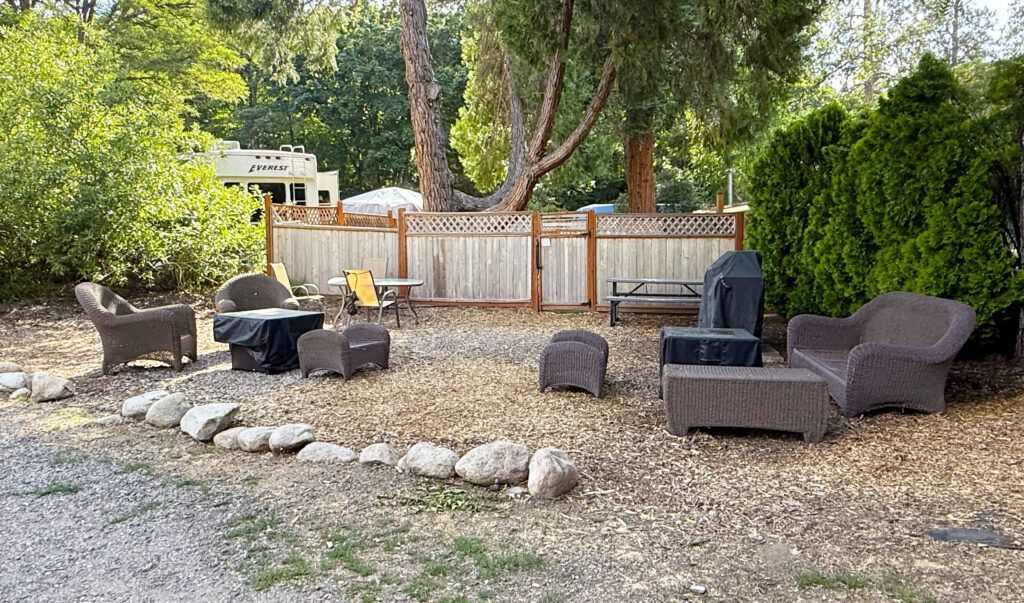 Backyard fire pit area with gravel, outdoor chairs, and a wooden fence under trees