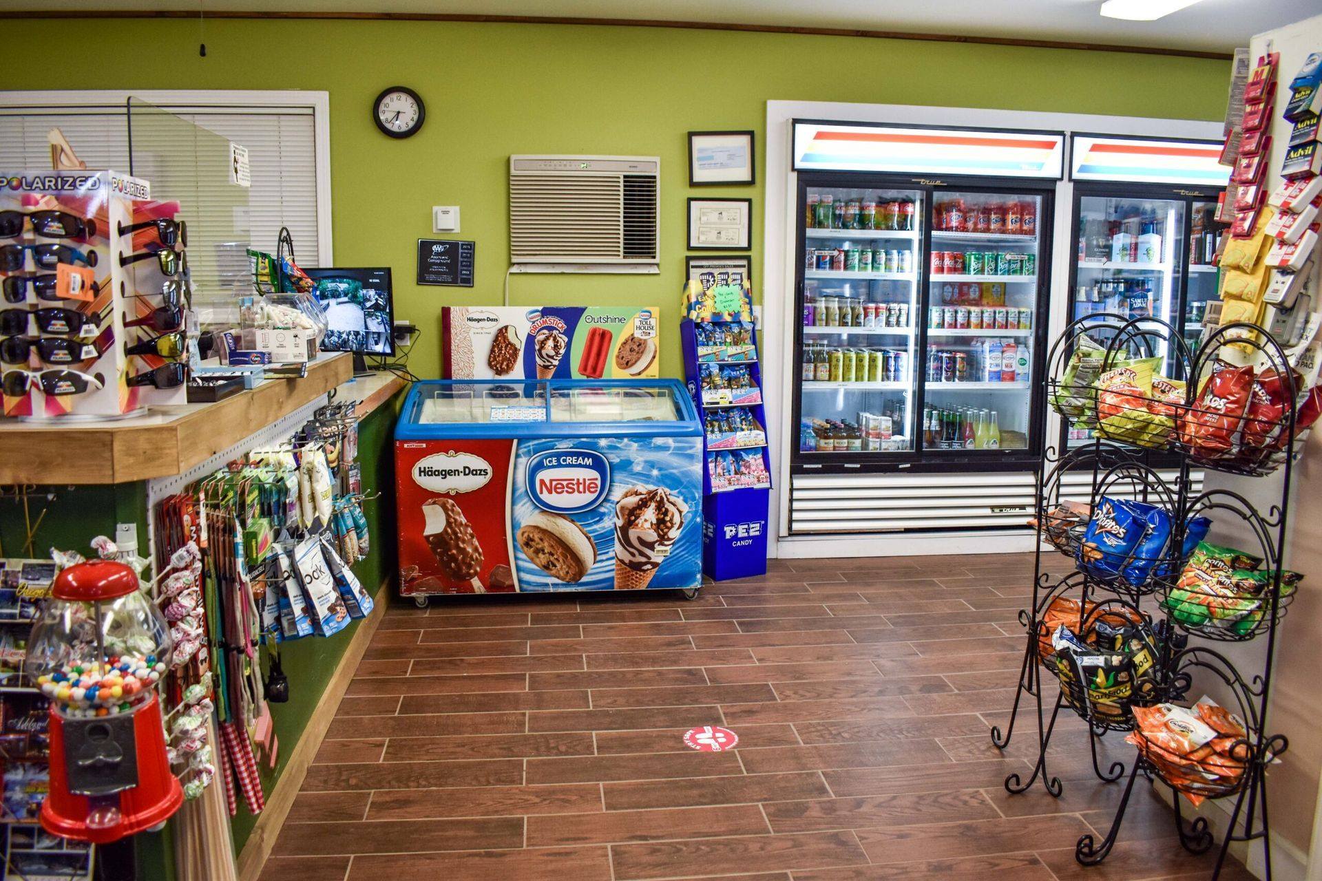 Convenience store aisle with drinks, snacks, and a glass-door refrigerator on tiled flooring
