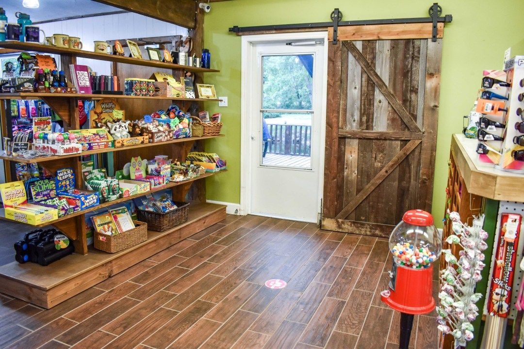 Small rustic shop interior with snack shelves, wooden floor, and a barn-style door.