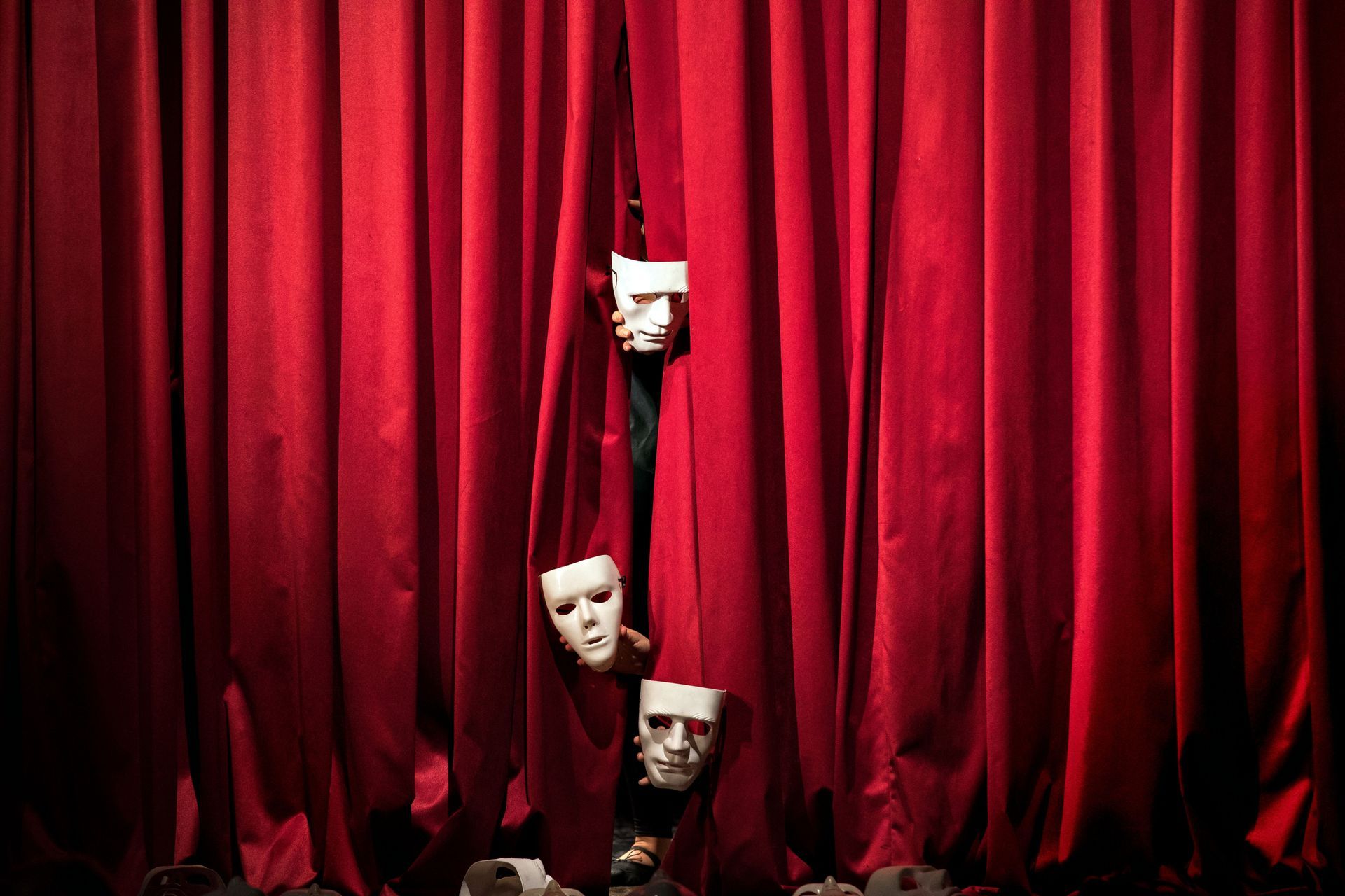 Red stage curtains with three theatrical masks peeking through