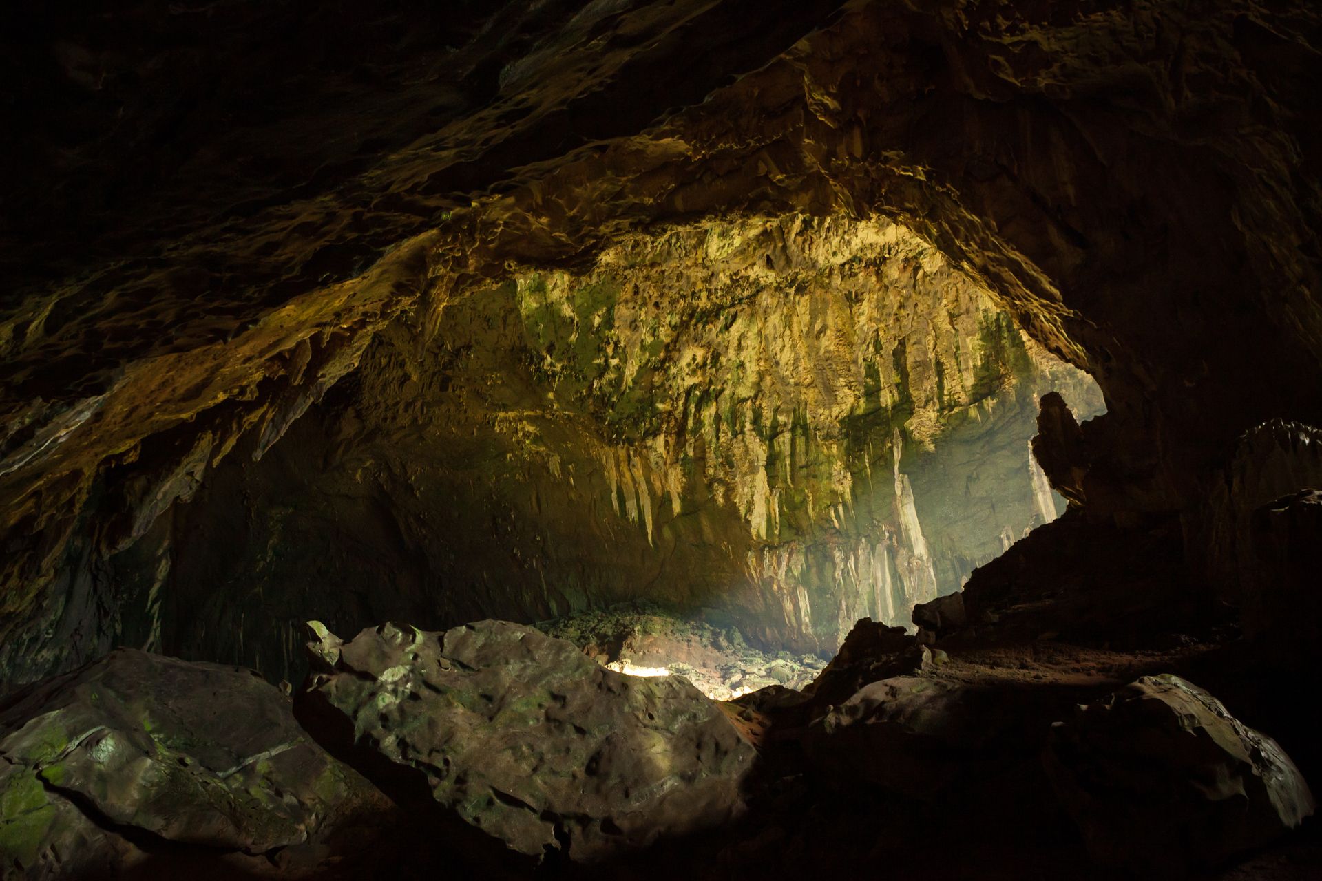 Sunlit cave with rocky floor and hanging formations, glowing golden against dark stone