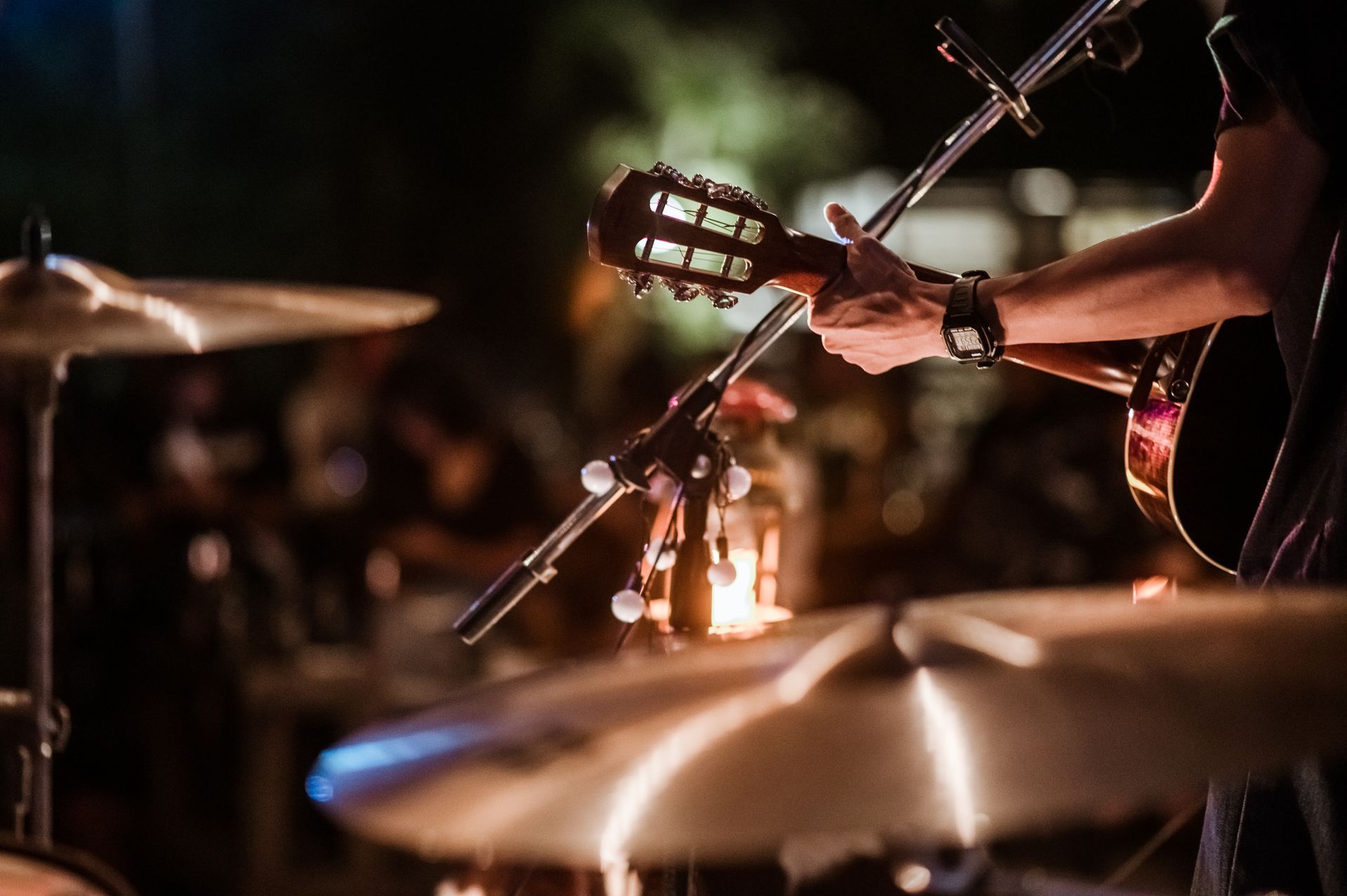 Musician playing guitar on a dimly lit stage with a drum cymbal in the foreground