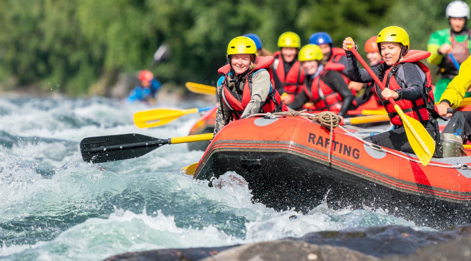 Group whitewater rafting in red raft, paddles raised through rough rapids with white spray