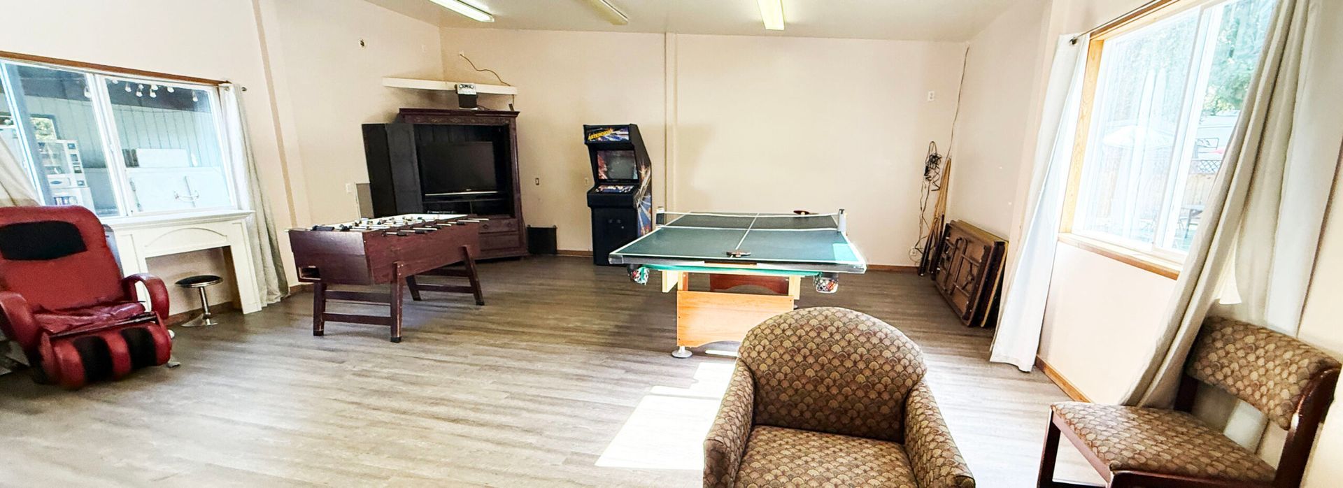 Spacious living room with a pool table, armchairs, TV, and large windows with blinds.