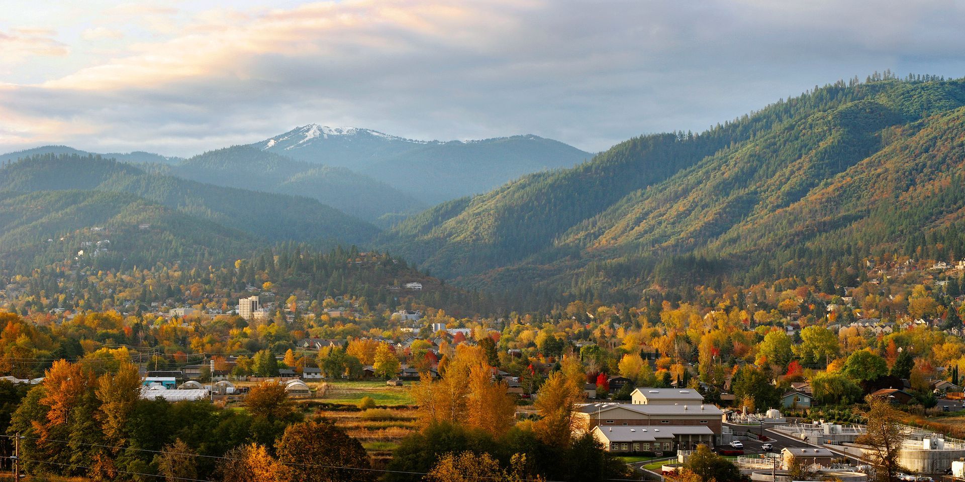 Autumn valley town with colorful trees, mountains, and misty hills under warm sunlight