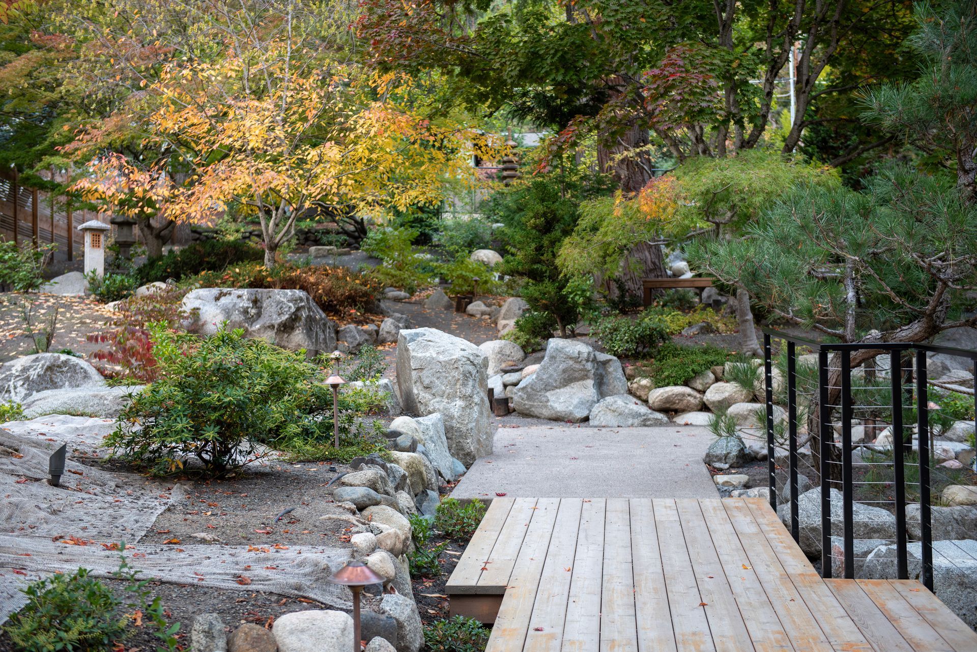 Rock garden with stone path, wooden bridge, and lush green trees in a landscaped yard