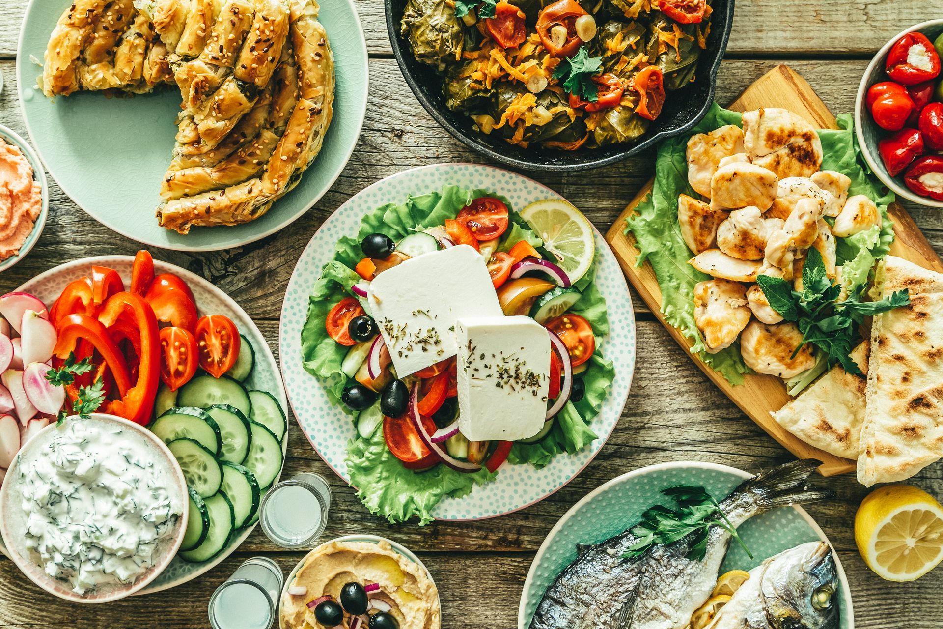 Assorted Mediterranean dishes arranged on a table, including salad, pita, hummus, cucumbers, tomatoes, and lemon.