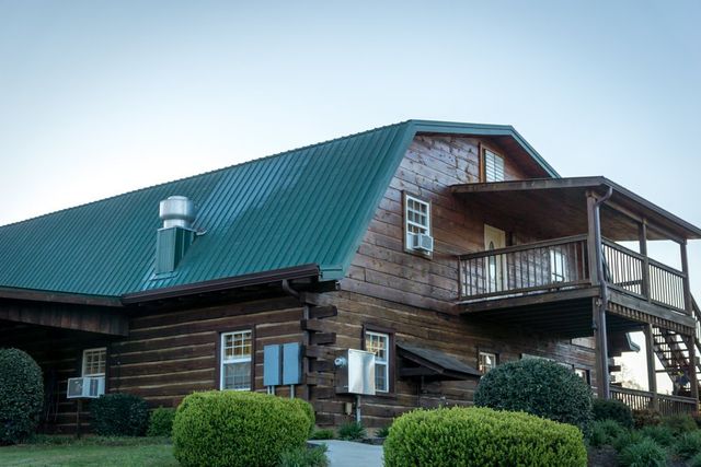 A large log lodge with a green roof and an upstairs porch