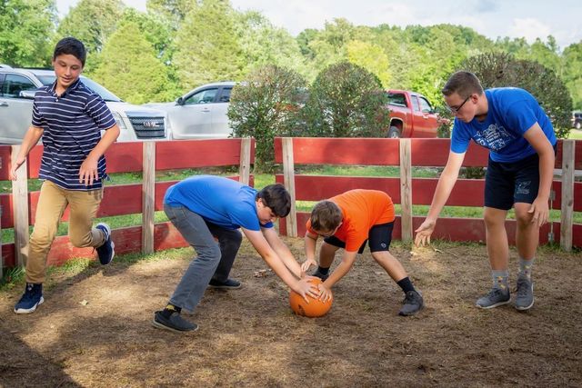 Four boys crouched around a ball in a fenced dirt ring