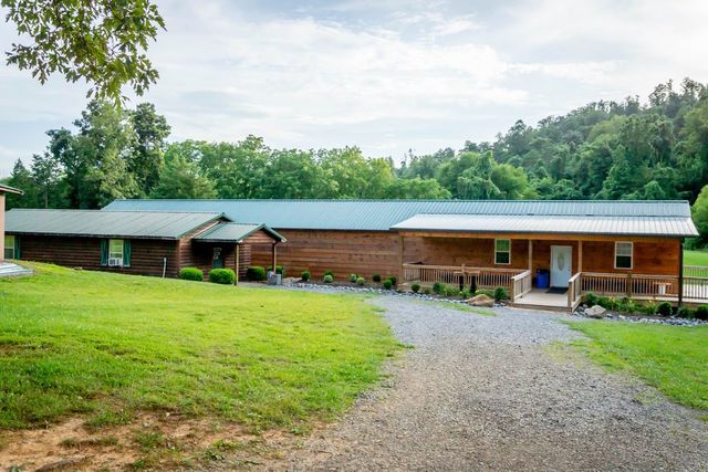 A long log building with a green roof beyond a lawn and gravel drive