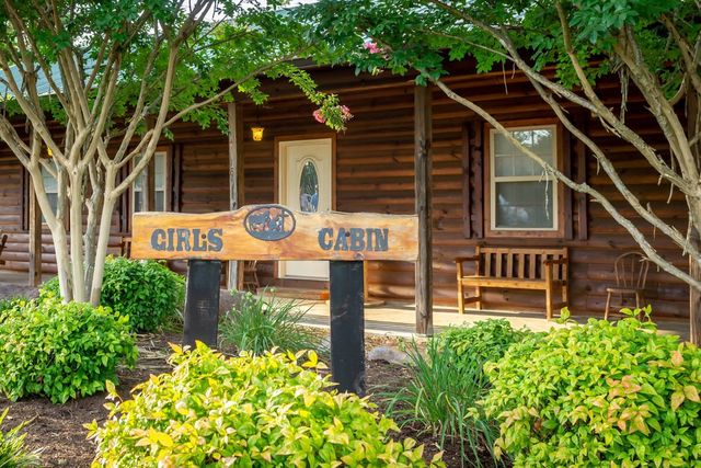 A carved Girls Cabin sign in front of a log cabin and flower beds