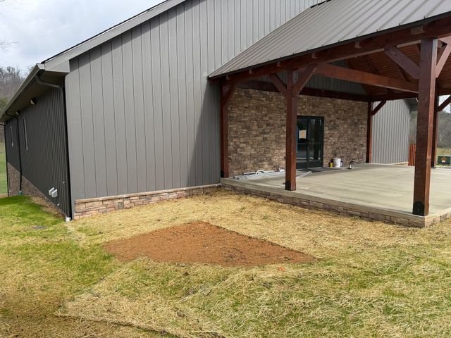 A gray metal building with a timber porch and fresh straw on the ground
