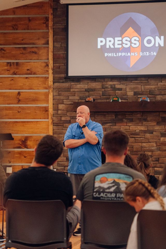 A preacher speaking to seated campers, a screen behind him