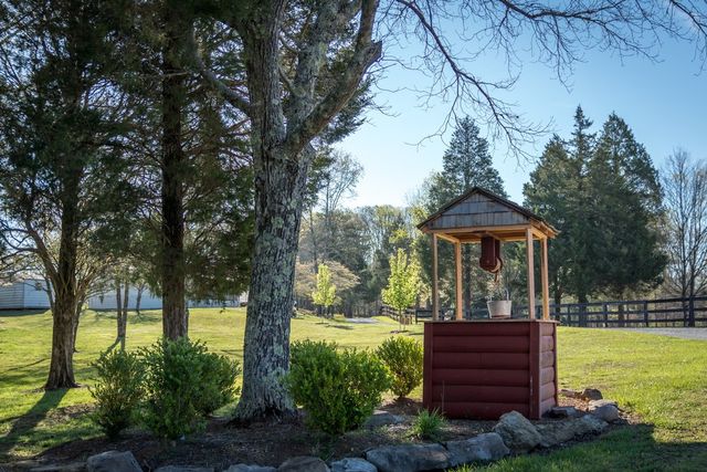 A small wooden gazebo on a lawn under tall trees