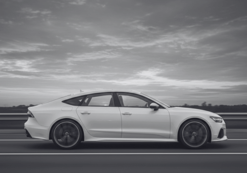 White Audi driving on a road under a cloudy sky, side view