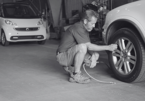 Mechanic crouching by a car tire in a garage, checking the wheel with a tool.