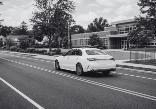 White Mercedes-Benz sedan driving past a school on a quiet neighborhood street