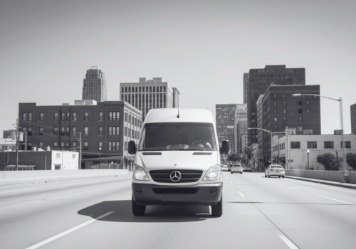 White van driving toward camera on a city bridge with skyline in the background
