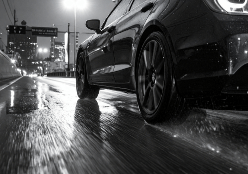 Black car driving on a wet city road at night, water spraying from tires.