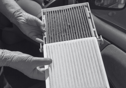 Hands holding a dirty cabin air filter beside a clean pleated filter in a car interior