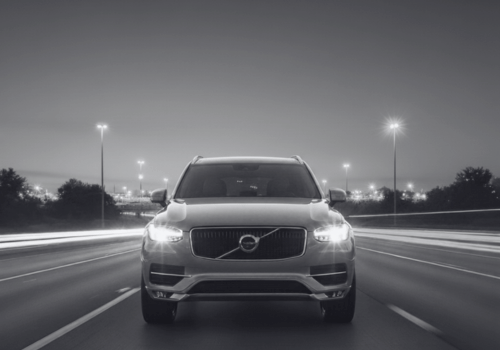 Front view of a silver Volvo SUV driving on a highway at night, headlights on.