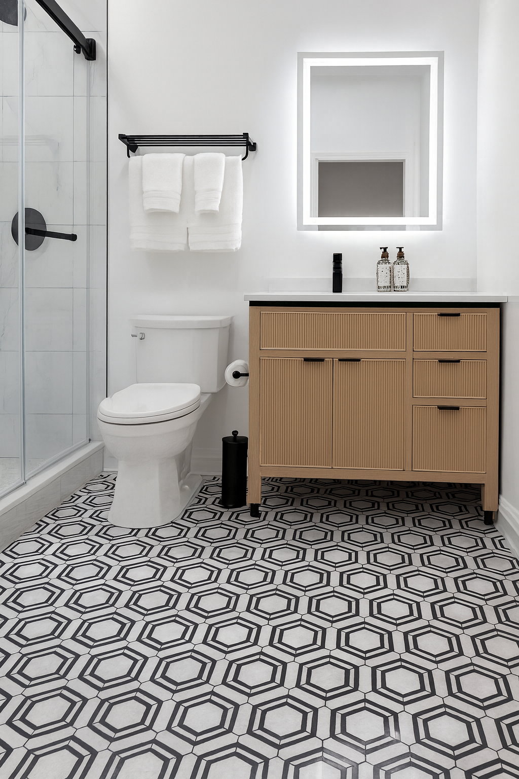 Bright modern bathroom with hexagon tile floor, glass shower, toilet, and wood vanity with mirror.