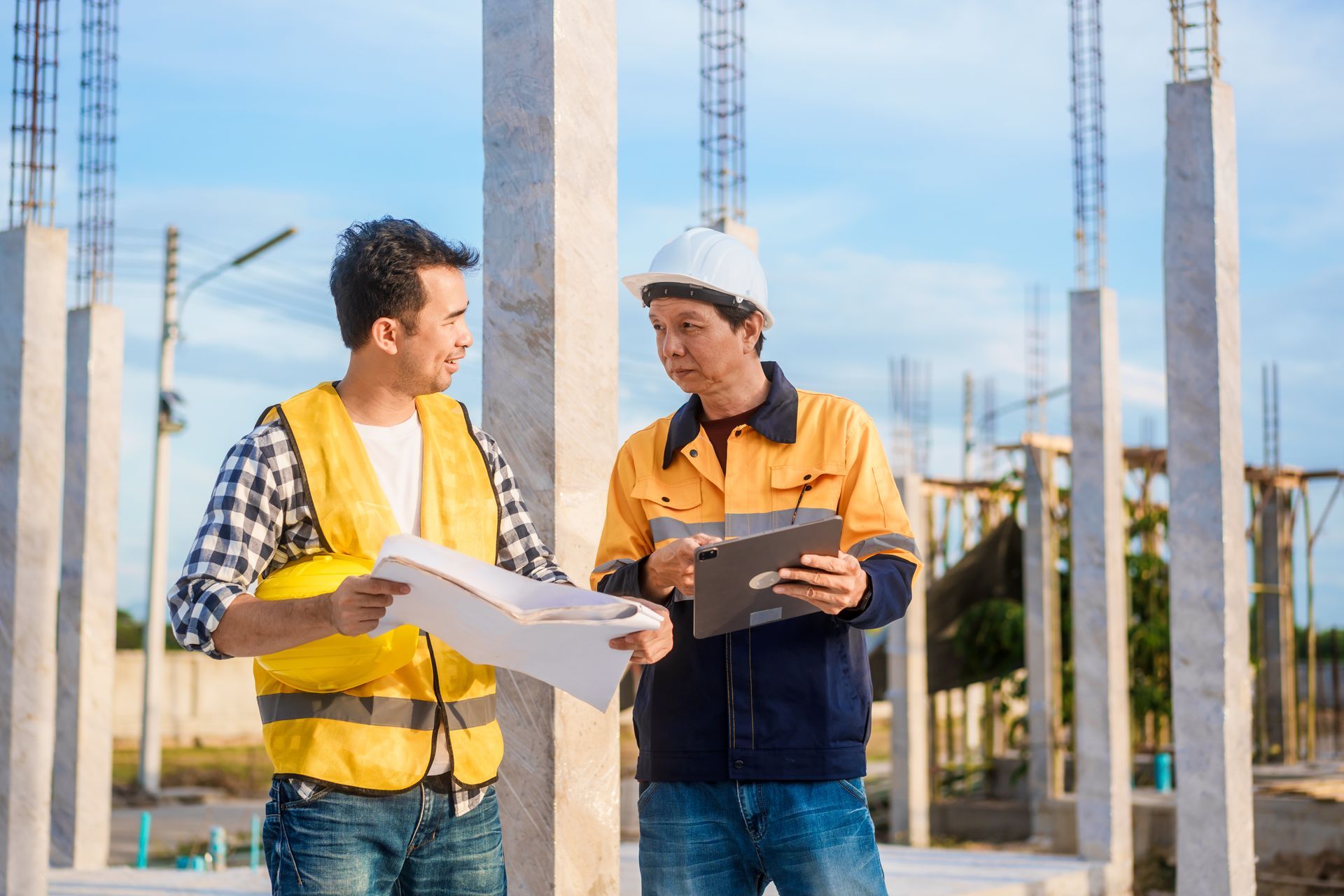 Two construction workers in safety vests reviewing blueprints at a building site Two construction workers in safety vests reviewing blueprints at a building site