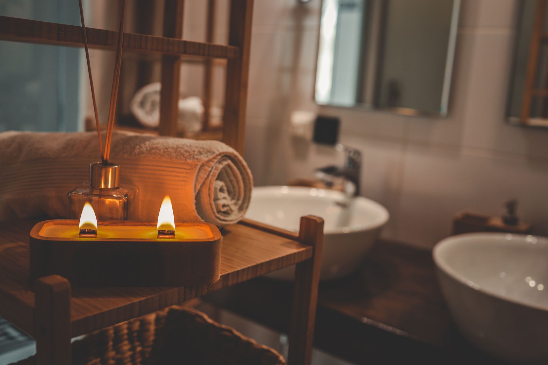 Spa room with lit candles, rolled towels, and sinks in a warm, dimly lit bathroom