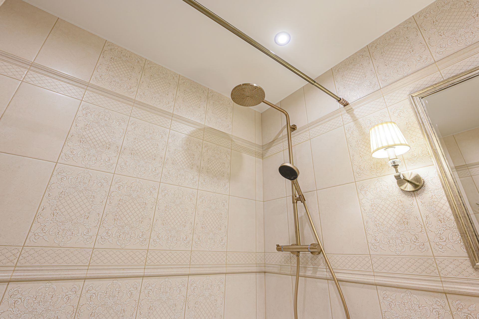 Bathroom shower with tiled walls, handheld showerhead, and lit wall sconce in a corner.