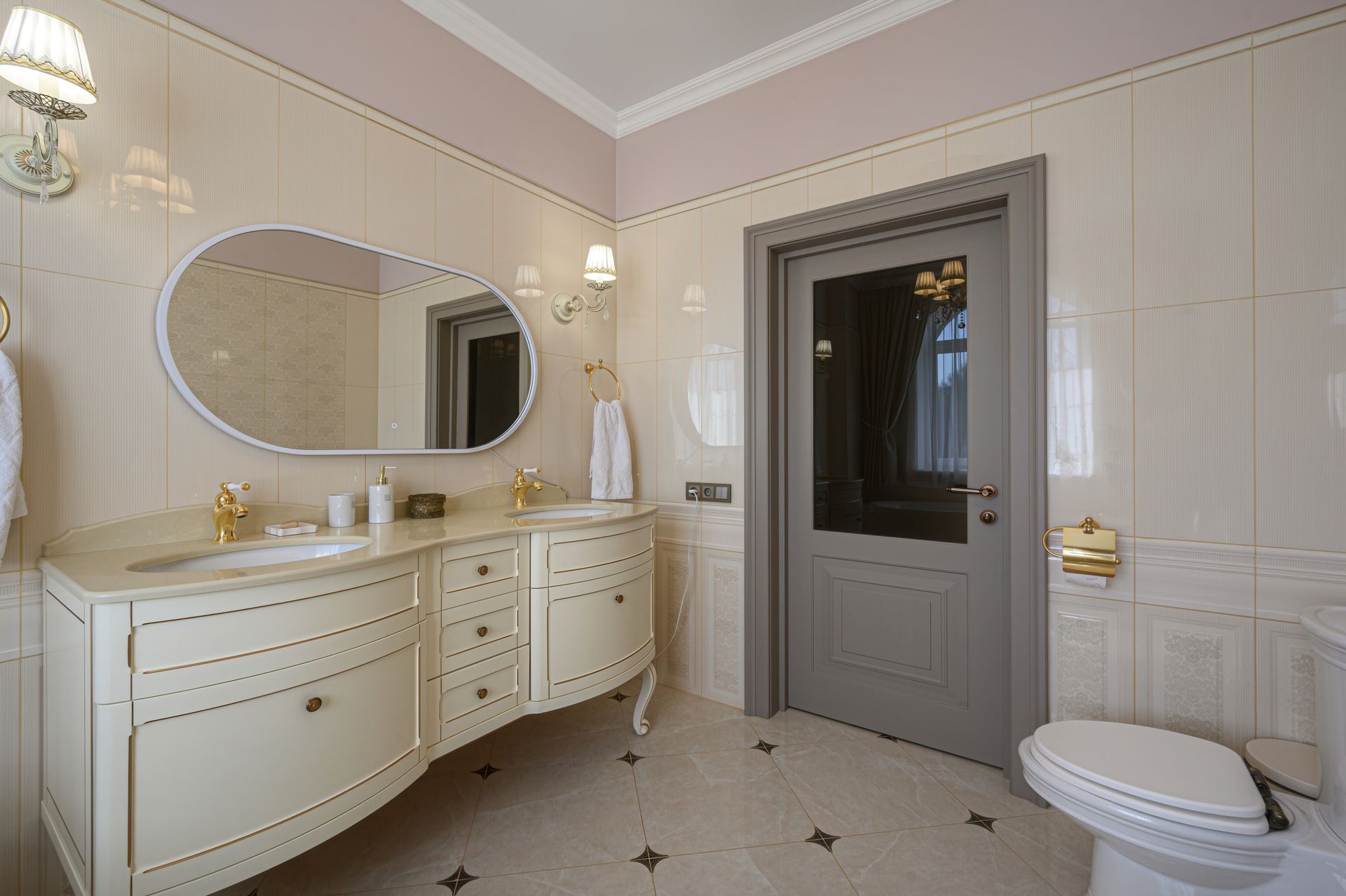 Elegant bathroom with cream walls, oval mirror, white vanity, gray door, and toilet. Elegant bathroom with cream walls, oval mirror, white vanity, gray door, and toilet.