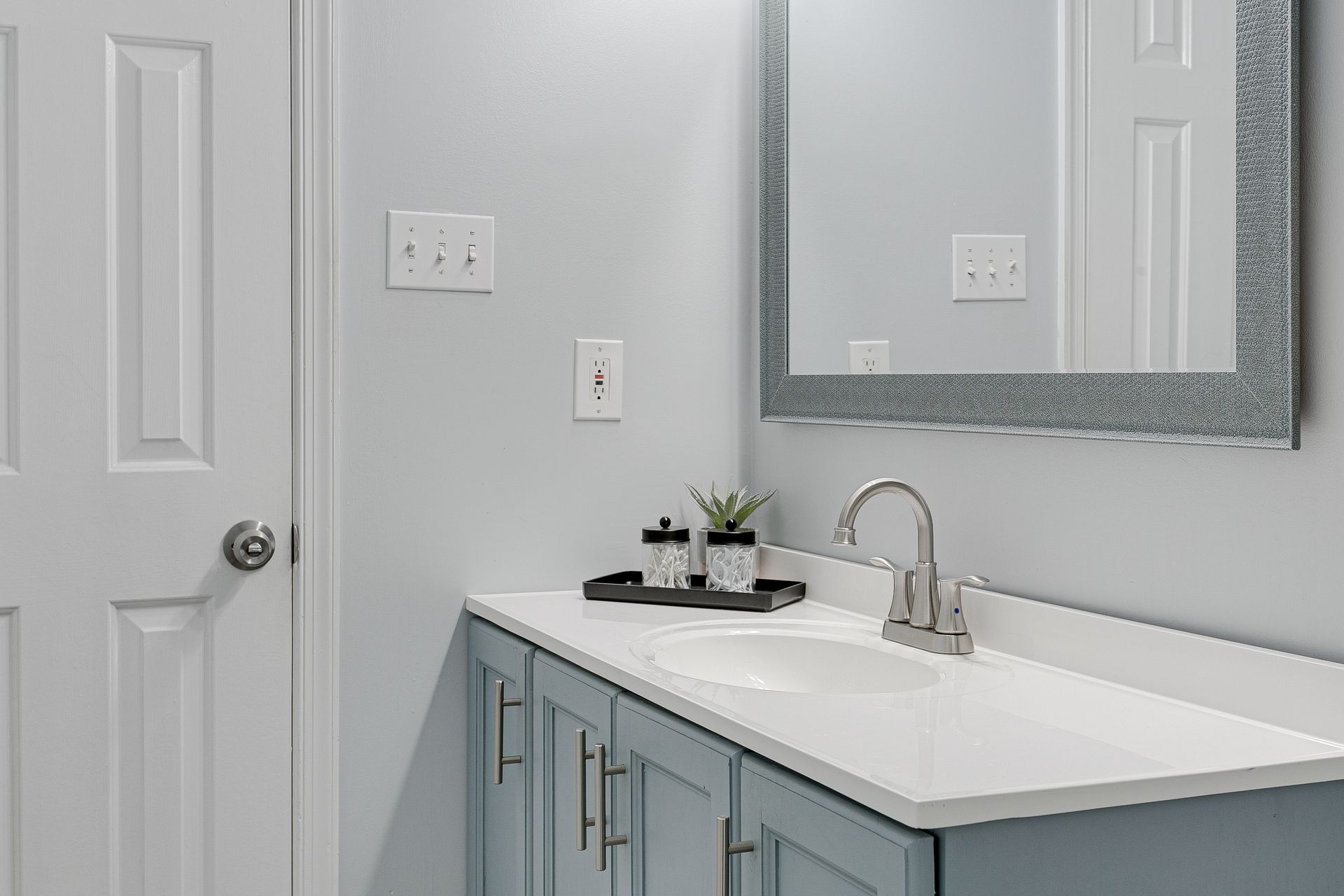 Bright white bathroom with a blue vanity, sink, mirror, and closed door Bright white bathroom with a blue vanity, sink, mirror, and closed door