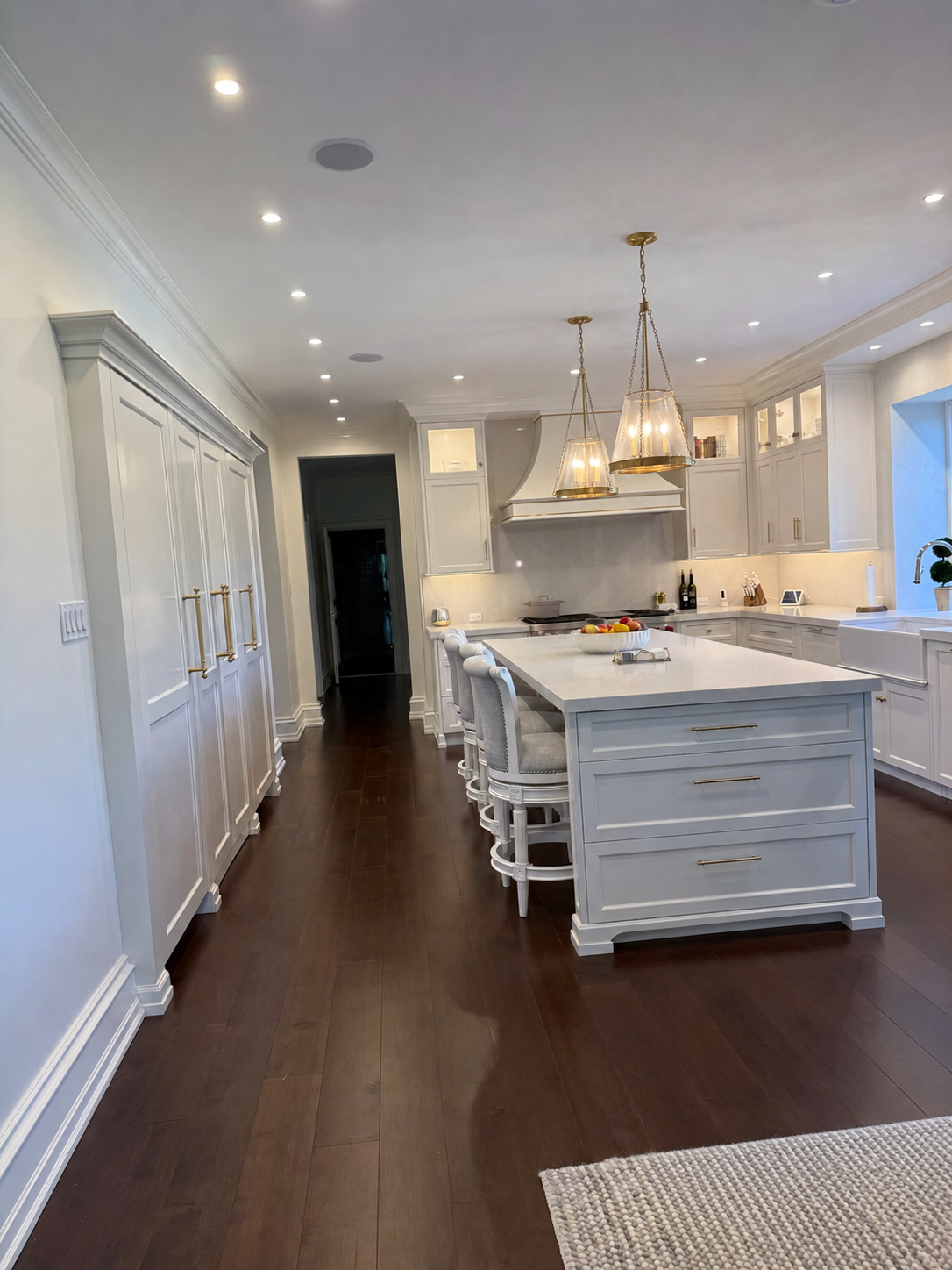 Bright white kitchen with marble island, pendant lights, dark wood floors, and built-in cabinets Bright white kitchen with marble island, pendant lights, dark wood floors, and built-in cabinets
