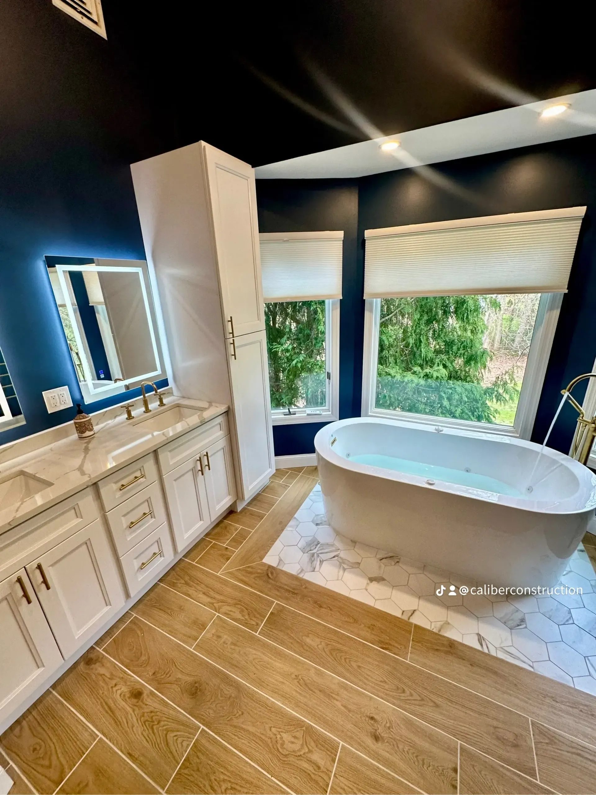 A bathroom with a tub, sink, mirror and window.