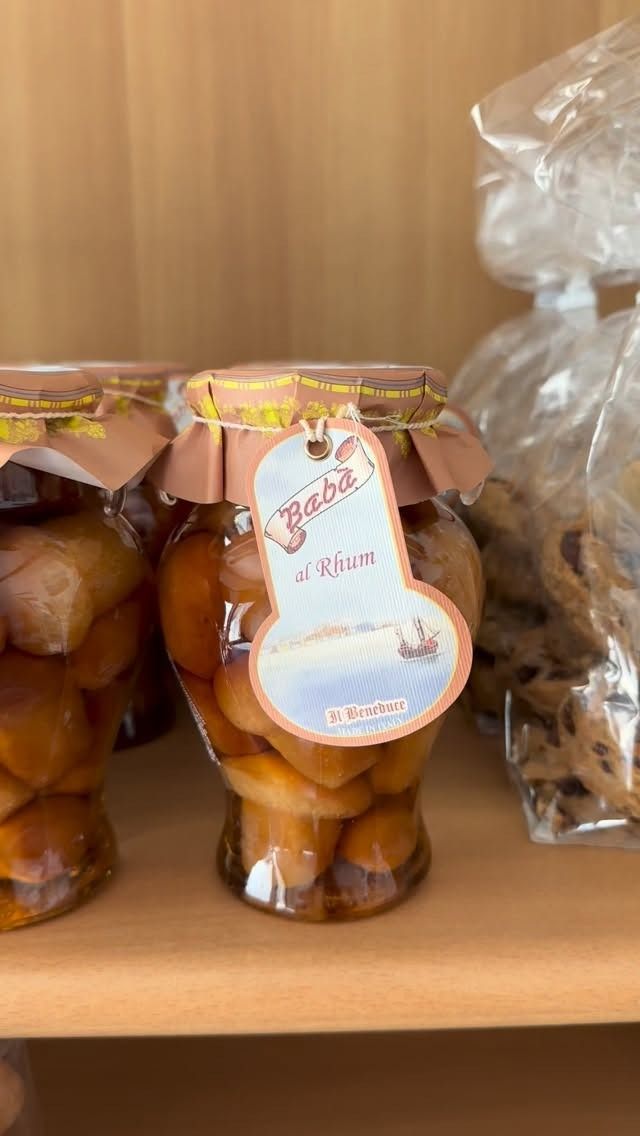 Barattoli di vetro contenenti conserve fatte in casa, legati con nastri rosa, su uno scaffale di legno.