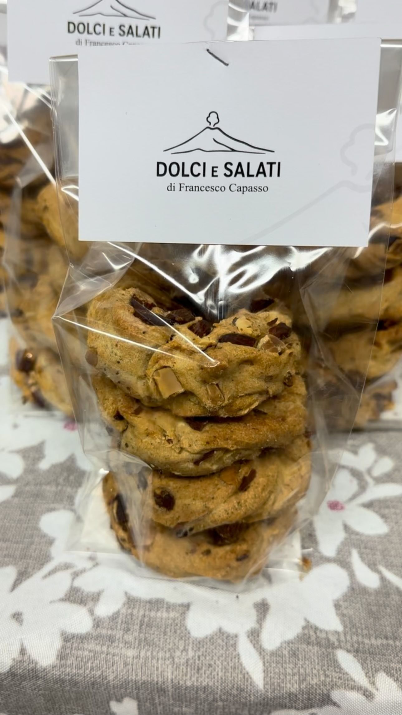 Sacchetto trasparente di biscotti con gocce di cioccolato e un'etichetta bianca Dolce Salati su una tovaglia a fantasia.