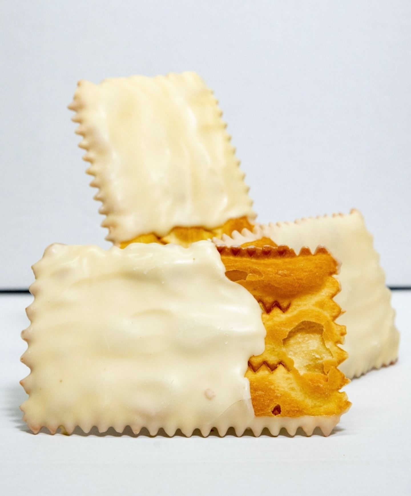 Biscotti sandwich con glassa bianca impilati su uno sfondo chiaro, uno dei quali mostra una farcitura di crema dorata.
