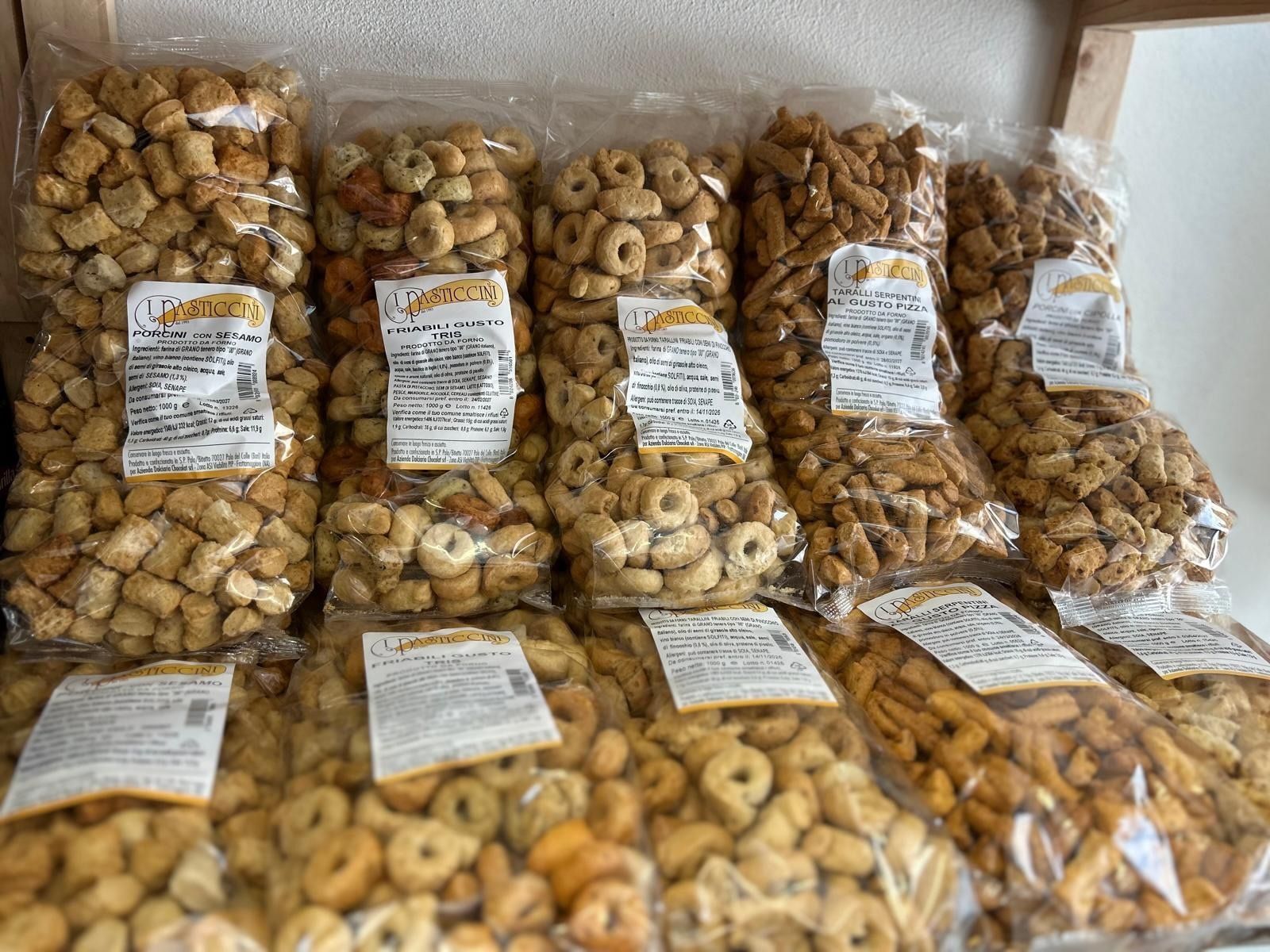 Snack assortiti confezionati in sacchetti di plastica trasparente, impilati su uno scaffale, con etichette su ogni sacchetto.