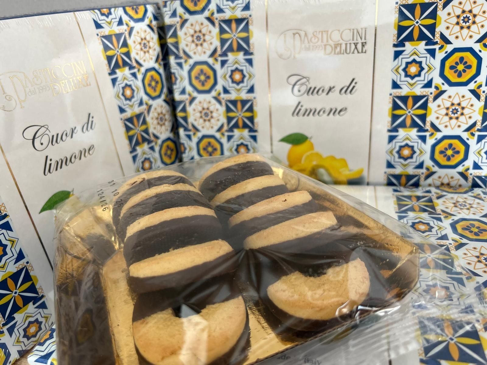 Biscotti al limone assortiti in confezione trasparente con scatole blu decorate sullo sfondo.