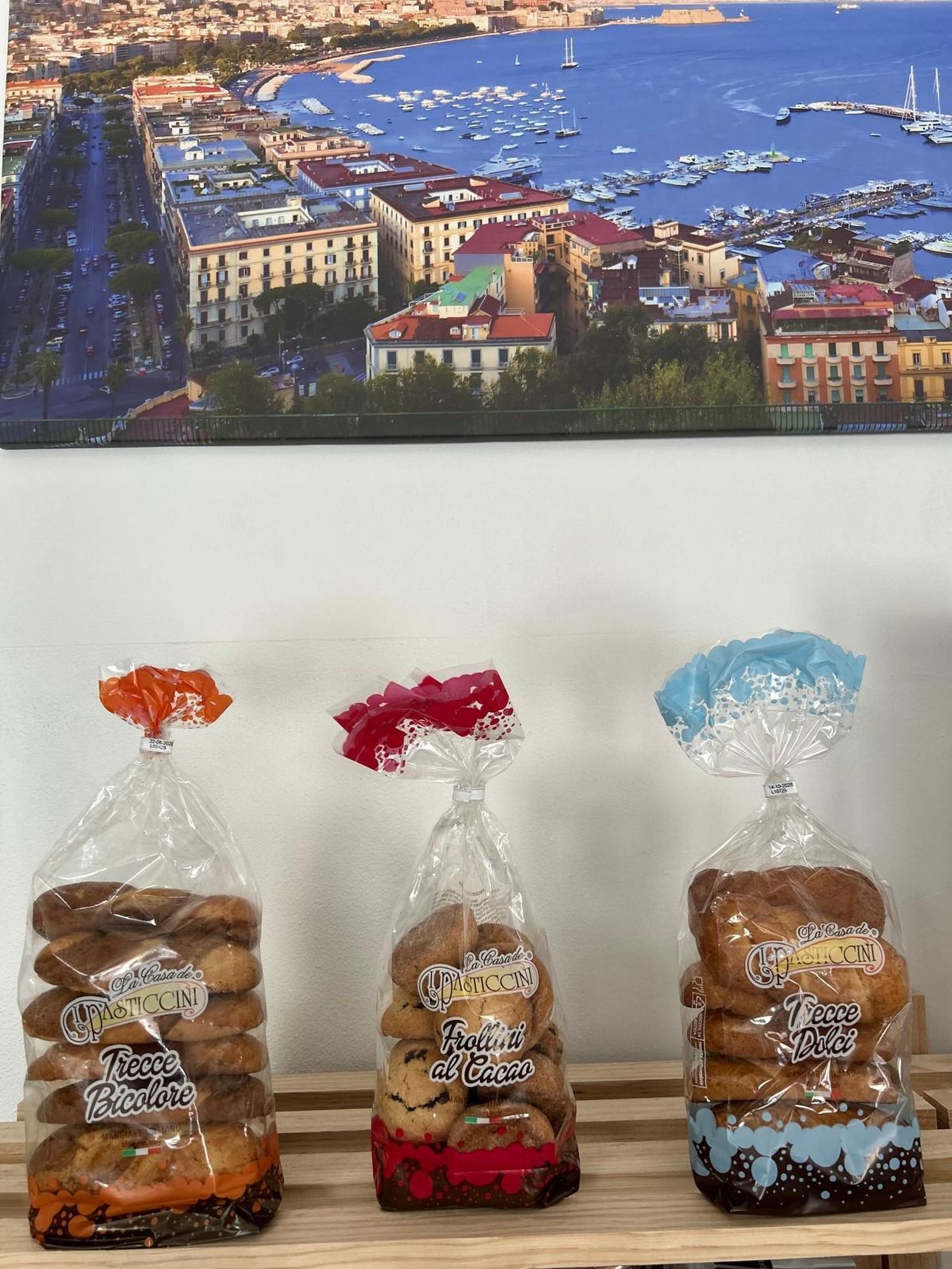 Tre barattoli decorativi per biscotti avvolti in plastica trasparente, sotto la stampa di una foto di una città costiera.