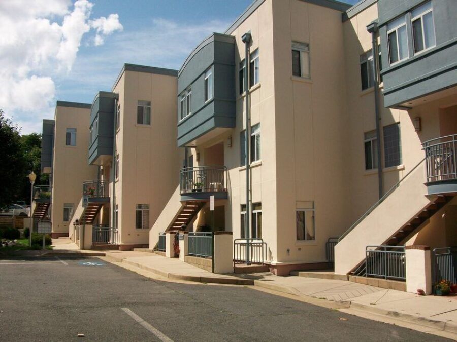 Row of beige apartment buildings with exterior staircases along a paved street