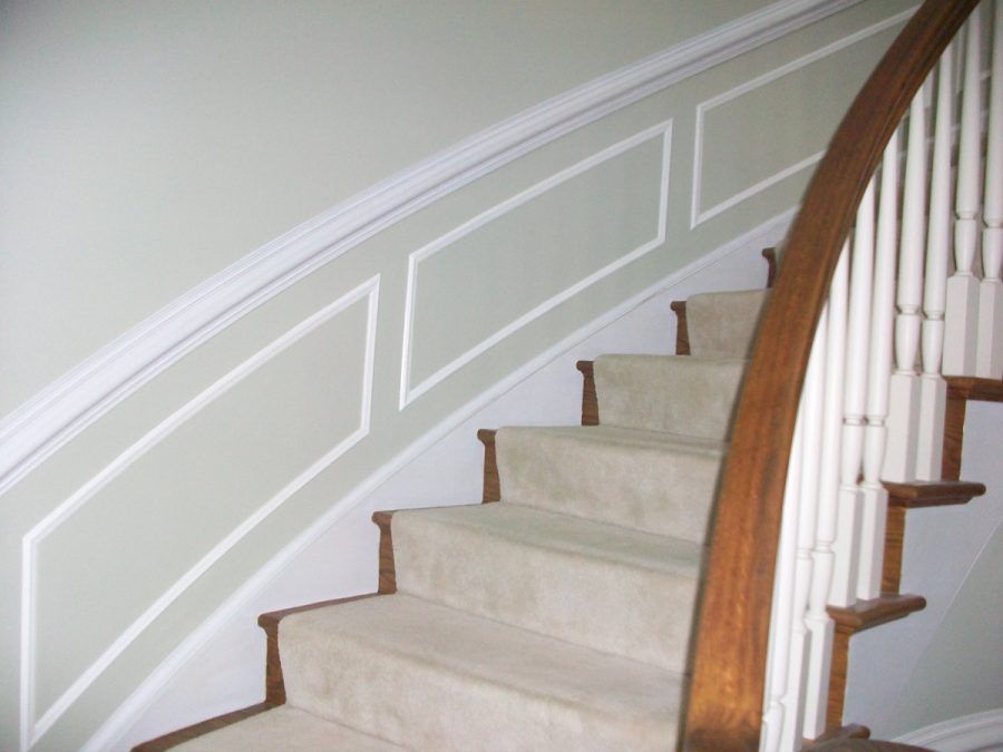 Carpeted staircase with white wall paneling and a wooden banister in a home interior