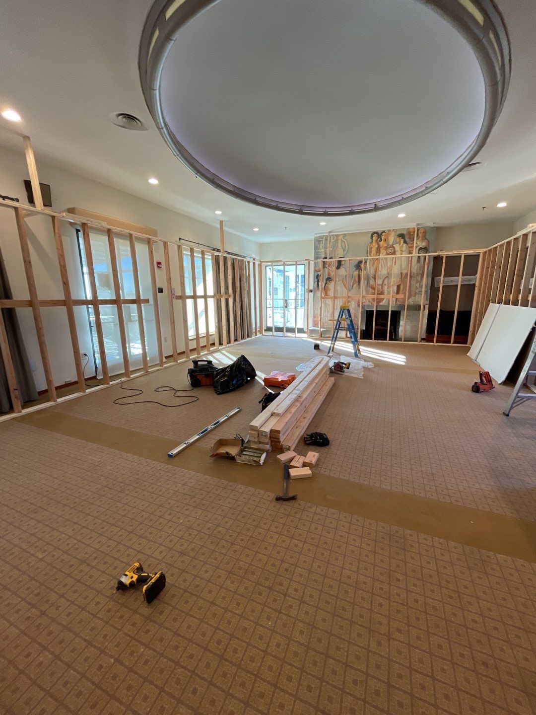 Large unfinished room with exposed walls, scattered tools, and a ladder under a circular ceiling feature