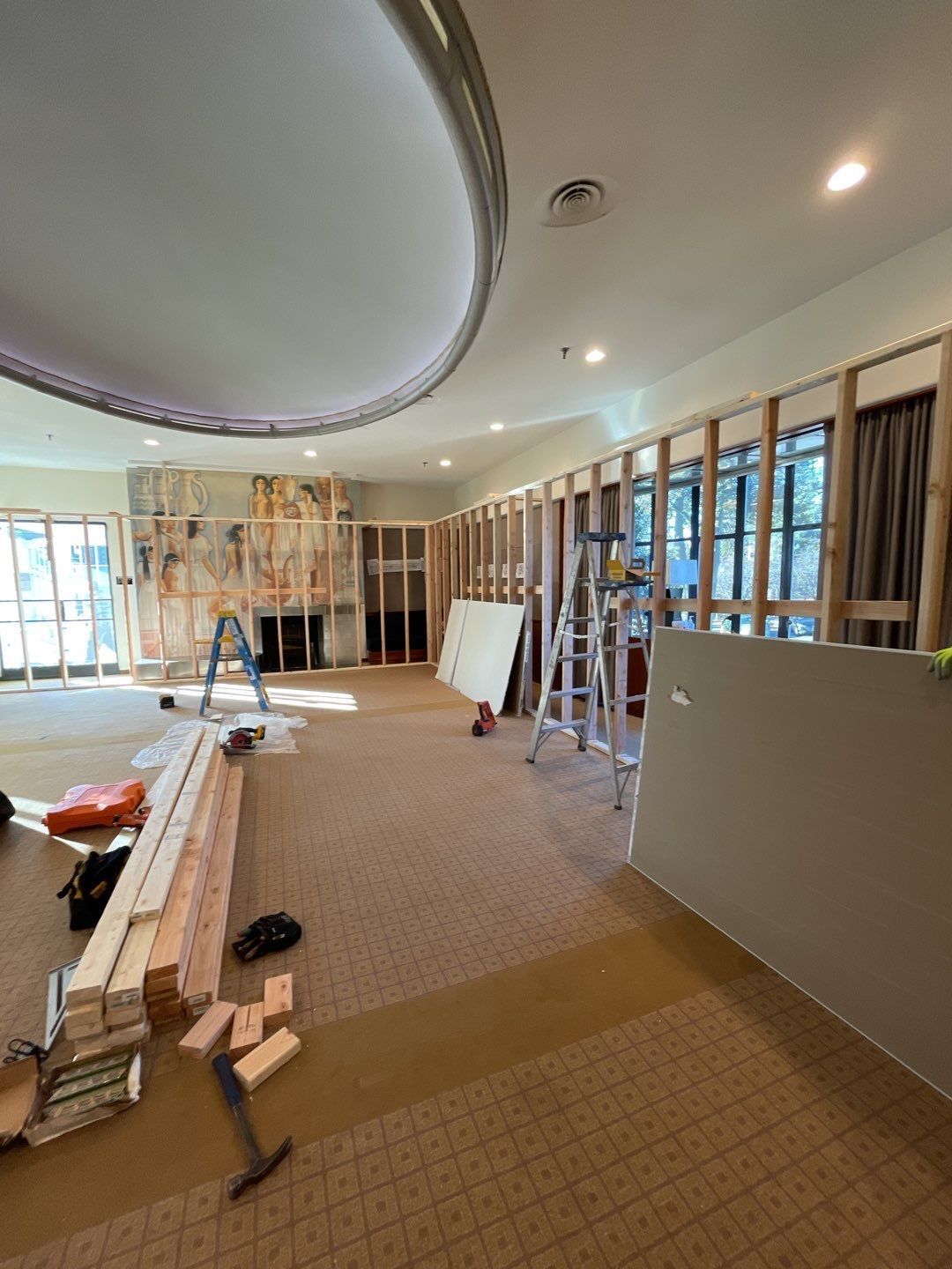 Partially renovated room with exposed framing, ladders, and construction materials under a curved ceiling