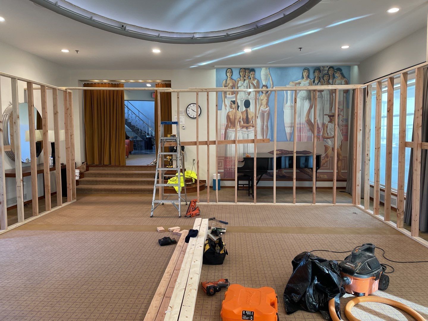 Indoor room under construction with exposed wall framing, tools, and materials on the floor.
