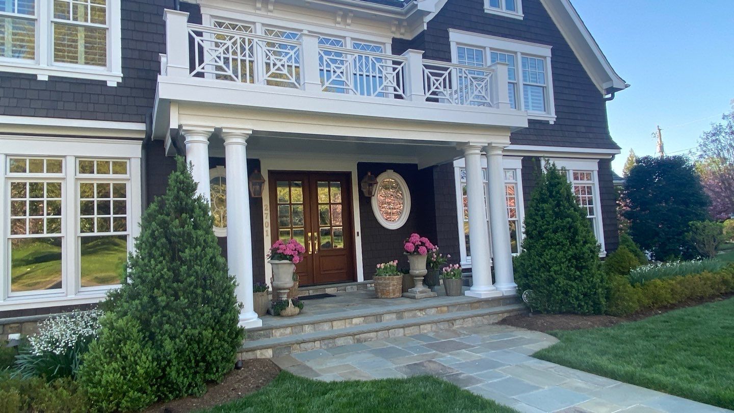 Large house with white columns, front porch, potted flowers, and a walkway leading to the entrance