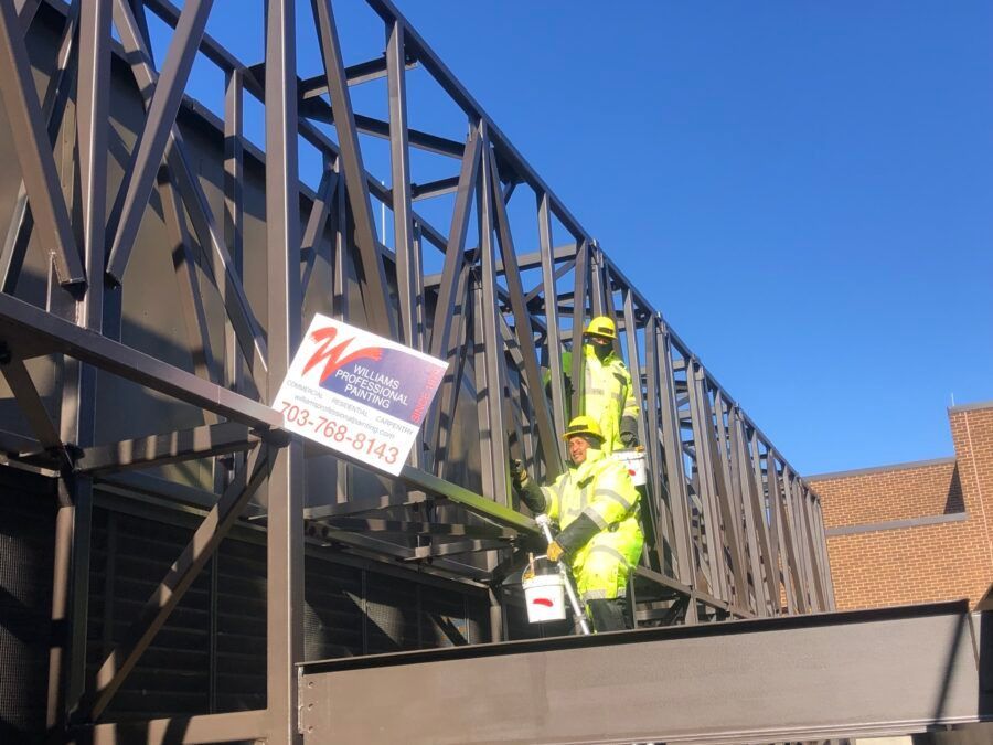 Workers in neon safety gear on a rooftop beside a metal truss, lifting a sign or panel.