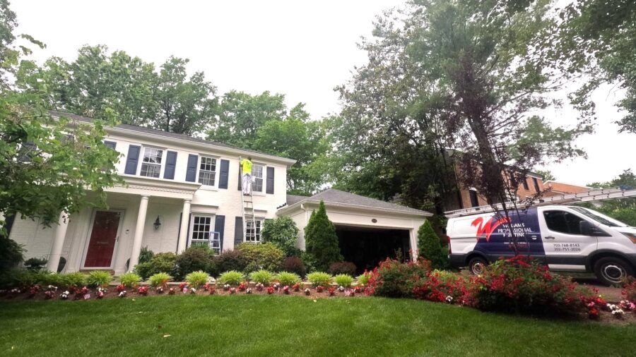 Suburban house with white columns, red flowers, and a van parked in the driveway under cloudy skies